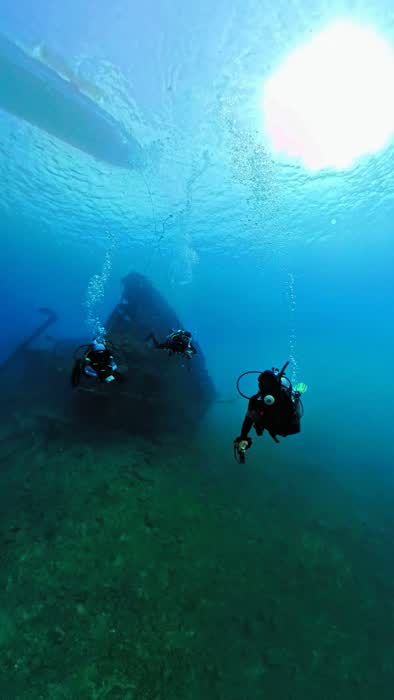 Two divers in blue water beneath the silhouetted hull of the dive boat