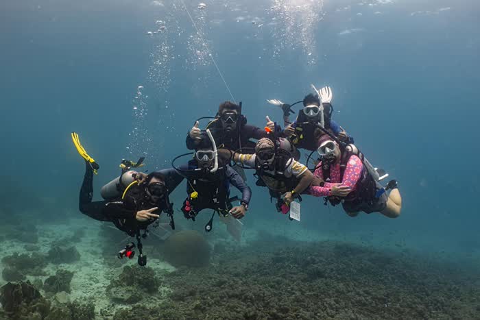 A group of divers posing together underwater above the reef