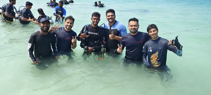 A group of divers standing together in shallow water off the beach